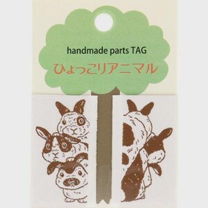 Puede incluir: Etiquetas de tela blanca con ilustraciones de animales marrones. Las etiquetas presentan un encabezado verde en forma de nube con el texto "handmade parts TAG" y texto japonés. La parte inferior de la etiqueta tiene el texto japonés "うさぎ 白".