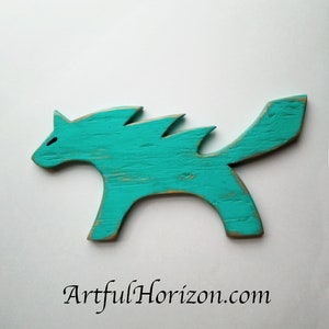 May include: A turquoise wooden cat figurine with a distressed finish. The cat has a stylized design with pointed ears and a curved tail. The figurine is painted turquoise with visible wood grain and a website address at the bottom.