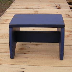 Puede incluir: Un peque&ntilde;o taburete de madera azul marino con una parte superior rectangular y una viga de soporte inferior. El taburete tiene un acabado envejecido, lo que sugiere un estilo vintage o r&uacute;stico. La direcci&oacute;n del sitio web "www.artfulhorizon.com" es visible.