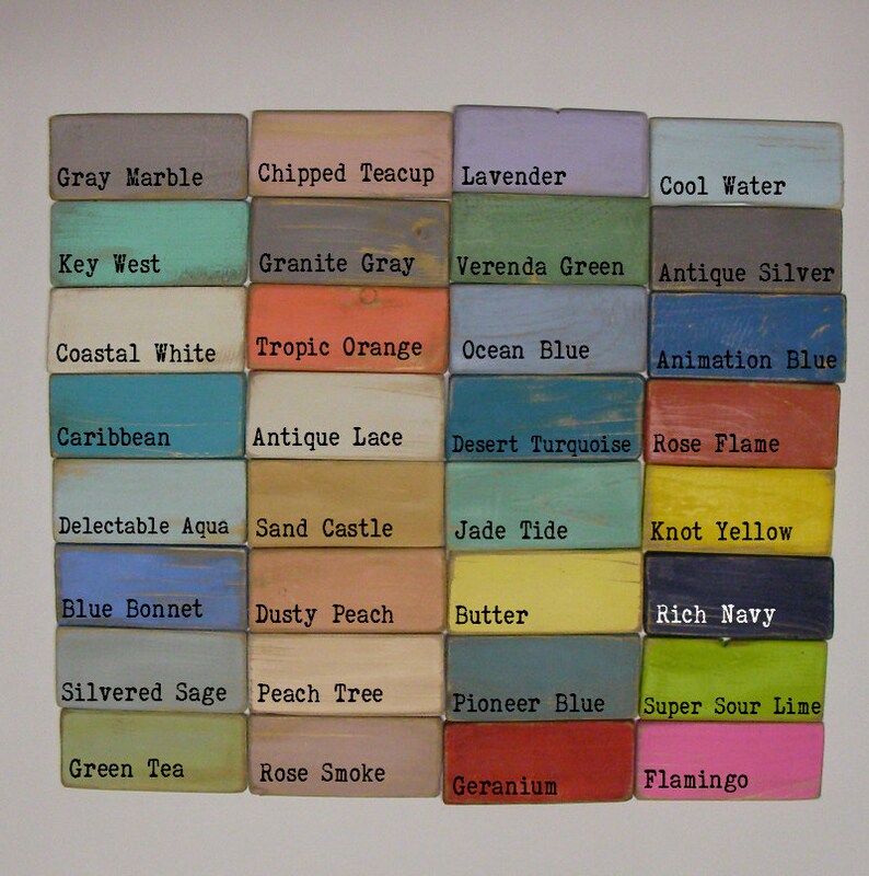 Puede incluir: Una colecci&oacute;n de bloques de madera pintados en varios colores, cada uno etiquetado con un nombre de color. Los colores incluyen "Gray Marble", "Lavender", "Ocean Blue", "Rose Flame" y "Flamingo". Los bloques tienen una apariencia desgastada y r&uacute;stica.