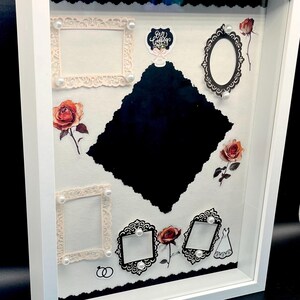 May include: White shadow box with a variety of decorative elements. Includes ornate frames, pearl accents, and floral stickers. Features a large black diamond-shaped cutout and the text "Our Wedding".