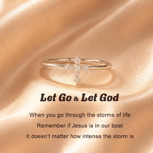 May include: A thin silver-toned ring featuring a small cross centerpiece adorned with five clear stones. The text reads: Let Go & Let God. When you go through the storms of life. Remember if Jesus is in our boat. It doesn't matter how intense the storm is.