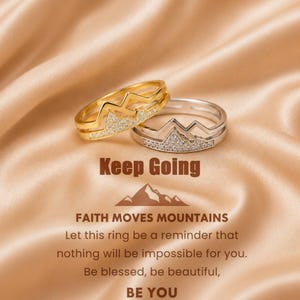 May include: Two rings, one gold-toned and one silver-toned, each featuring a mountain range silhouette accented with small clear stones. The text reads: Keep Going, FAITH MOVES MOUNTAINS, Let this ring be a reminder that nothing will be impossible for you. Be blessed, be beautiful, BE YOU.