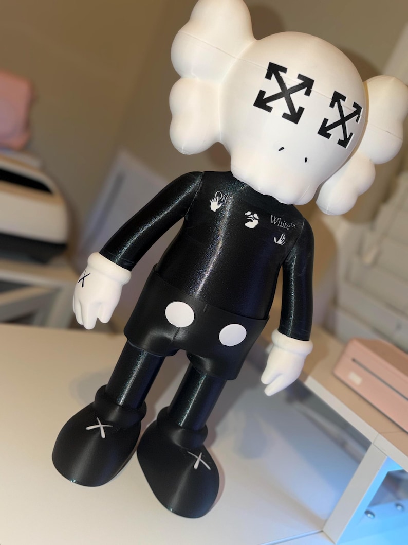 May include: A black and white figurine with a skull-shaped head and crossed-out eyes. The figurine has a black body, shorts with white circles, and white gloves. The feet have white crosses. The word "White" is printed on the chest.