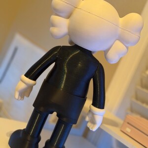May include: A black and white figurine of a cartoon character with a rounded head and crossbones on the back. The figure is wearing a black outfit with white gloves and shoes. The figurine is standing on a white surface.