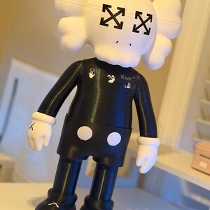 May include: A black and white figurine with a skull-shaped head and crossed-out eyes. The figurine wears a black outfit with white gloves and shoes. The text "White" is visible on the chest.