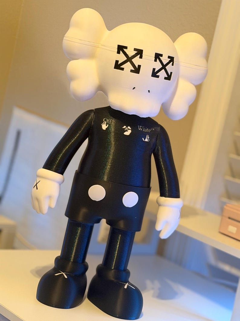 May include: A black and white figurine with a skull-shaped head and crossed-out eyes. The figurine wears a black outfit with white gloves and shoes. The text "White" is visible on the chest.