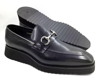 Mocasines de hombre de piel negra con detalle de estribo y hebilla plateada, zapatos de vestir de punta cuadrada.