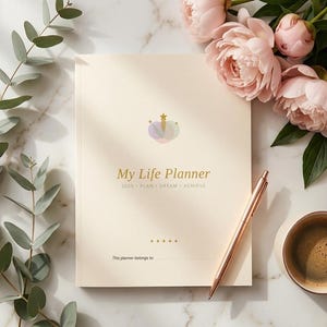 Peut inclure: Un agenda de couleur crème avec une icône de couronne et le texte My Life Planner 2025 PLAN DREAM ACHIEVE imprimé sur la couverture. Sous le texte se trouve une ligne pour l'identification. Un stylo en or rose repose sur la couverture.