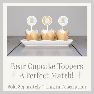May include: Three brown cupcake liners with white paper cupcake toppers featuring a brown bear silhouette on a light blue circle. The text "Bear Cupcake Toppers * A Perfect Match! * Sold Separately * Link in Description" is below the cupcakes.