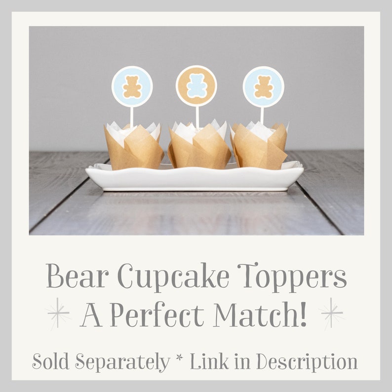 May include: Three brown cupcake liners with white paper cupcake toppers featuring a brown bear silhouette on a light blue circle. The text "Bear Cupcake Toppers * A Perfect Match! * Sold Separately * Link in Description" is below the cupcakes.