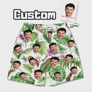 Pode incluir: Calções de banho brancos com um padrão repetitivo de folhas tropicais verdes, flores de orquídea cor-de-rosa e o rosto de um homem. Os calções têm um cordão branco na cintura. O texto "Custom" e "Put your face on it" aparece acima.