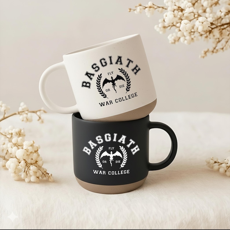 May include: Two ceramic mugs stacked vertically. The top mug is off-white with black text reading Basgiath War College and a dragon graphic. The bottom mug is black with white text reading Basgiath War College and a dragon graphic. Both have tan bases.