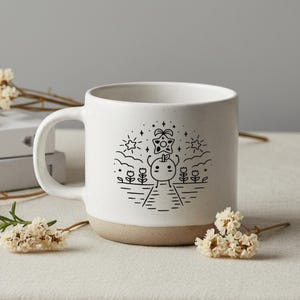 Peut inclure: Mug en c&eacute;ramique blanche avec une base beige et un dessin au trait noir fantaisiste. L'illustration repr&eacute;sente un personnage de dessin anim&eacute; avec une t&ecirc;te de pomme, une &eacute;toile, des fleurs et un chemin. La tasse a une grande anse.