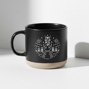 Peut inclure: Mug en c&eacute;ramique noire avec une base beige et une anse noire. Le mug pr&eacute;sente un dessin blanc d'un personnage avec un cadeau, des fleurs, des &eacute;toiles et un soleil. Convient aux boissons chaudes ou froides.