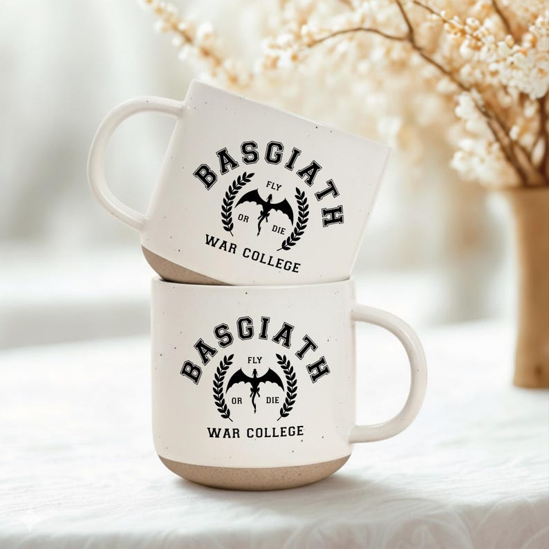 May include: Two stacked off-white ceramic mugs with a speckled finish and a tan base. Each mug features a black graphic with the text "BASGIATH WAR COLLEGE" in a circular layout, surrounding a central dragon silhouette and the words "FLY OR DIE".