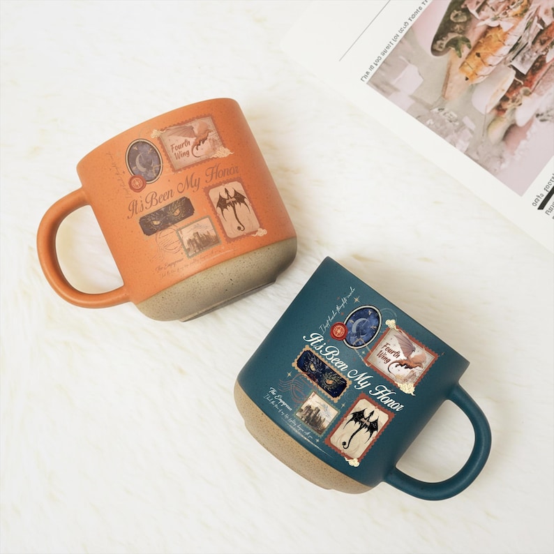 May include: Two ceramic mugs, one orange and one dark teal, featuring a speckled beige base. Each mug displays the text "It's Been My Honor" alongside "Fourth Wing" and various graphic stamps including a dragon, a moon, and castle imagery.