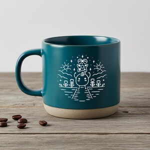 Peut inclure: Mug en c&eacute;ramique bleu sarcelle avec une illustration blanche d'un personnage de dessin anim&eacute; avec une &eacute;toile au-dessus de sa t&ecirc;te, entour&eacute; d'&eacute;toiles et de fleurs. Le bas de la tasse est beige clair. Des grains de caf&eacute; sont sur une surface en bois.
