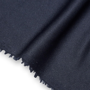 Könnte beinhalten: Ein Stück dunkelblauer Stoff mit einer feinen, gleichmäßigen Strickstruktur. Das Material ist gefaltet, um weiche, vertikale Falten zu erzeugen, und die Unterkante zeigt einen rohen, unfertigen und leicht ausgefransten Rand mit losen Fäden.