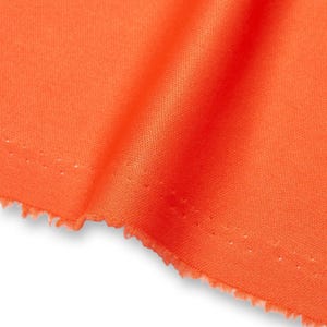 Könnte beinhalten: Ein leuchtend orangefarbener Stoff mit einer feinen, gleichmäßigen Webstruktur. Das Material ist gefaltet, um einen weichen, diagonalen Fall über die Oberfläche zu erzeugen, wobei eine rohe, leicht ausgefranste Kante am unteren Rand sichtbar ist.