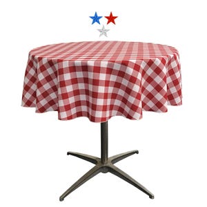 Op de afbeelding: Een ronde tafel met een rood-wit geruite tafelkleed. De tafel heeft een donker metalen voet met een stervormig ontwerp. Drie sterdecoraties bevinden zich boven de tafel.