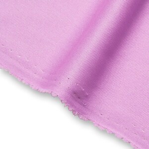 Op de afbeelding: Een stuk lichtpaarse stof met een fijne, uniforme maasstructuur. Het materiaal is gevouwen om zachte, vloeiende plooien te creëren, wat de consistente pastelkleur en de kleine, gelijkmatig verdeelde perforaties over het oppervlak benadrukt.