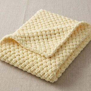 May include: A folded, cream-colored blanket with a woven texture. The blanket is made of a soft, plush material and is folded neatly, showcasing its intricate weave pattern. The blanket is a light, neutral color.