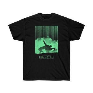 Puede incluir: Camiseta negra con un gráfico verde de la película "Matrix". El diseño muestra figuras en acción sobre un fondo de líneas verticales, con el título de la película debajo. La camiseta está hecha de un material suave.