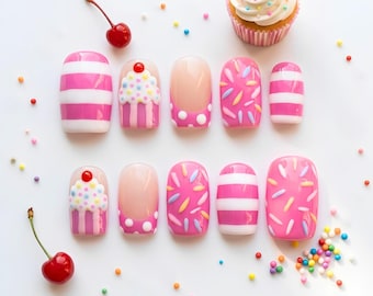 May include: A set of ten press-on nails featuring pink and white horizontal stripes, pink polka dots, raised cupcake designs with red cherries, and multi-coloured sprinkles. Two red cherries and scattered colourful sprinkles surround the nails.