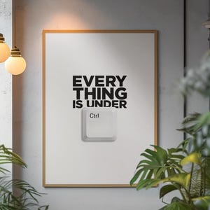 Op de afbeelding: Een rechthoekige wandprint in een lichthouten lijst met de zwarte tekst 'EVERY THING IS UNDER' boven een witte computertoetsenbordtoets met het label 'Ctrl'. Het ontwerp is gecentreerd op een witte achtergrond in de lijst.