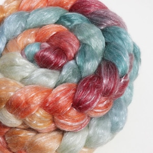 May include: A close-up of a circular braid of colorful yarn. The yarn is a mix of colors, including orange, red, teal, and blue. The braid is tightly woven and has a soft, textured appearance. The yarn is likely used for knitting or crocheting.