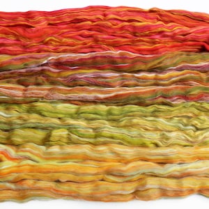 Op de afbeelding: Close-up van gekleurde vezels in tinten rood, oranje, geel en groen. De vezel is in horizontale lagen gerangschikt, waardoor een gradiënteffect ontstaat. De textuur lijkt zacht en golvend, wat suggereert dat het geschikt is om te spinnen of voor andere textielambachten.
