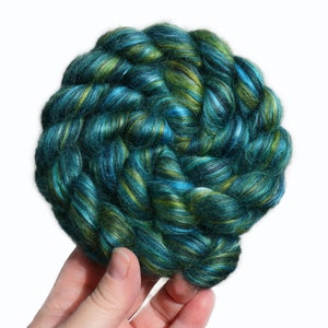 Peut inclure: Une pelote de fil teinte &agrave; la main de couleur turquoise, verte et blanche. Le fil est torsad&eacute; en cercle et est tenu dans une main.