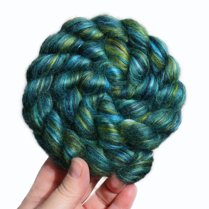 Peut inclure: Une pelote de fil teinte &agrave; la main de couleur turquoise, verte et blanche. Le fil est torsad&eacute; en cercle et est tenu dans une main.