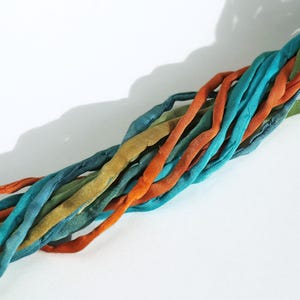 Op de afbeelding: Een close-up van een gevlochten koord gemaakt van meerdere strengen stof in tinten turquoise, groen en oranje.