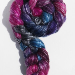 K&ouml;nnte beinhalten: Ein dicker, geflochtener Strang aus Spinnfaser in einer lebendigen Mischung aus Magenta, Dunkelviolett, K&ouml;nigsblau und Anthrazit. Die Faser hat einen gl&auml;nzenden, seidigen Schimmer und ist zu einer Kreisform mit einem langen Ende gewickelt.