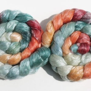 May include: Two spiral-shaped skeins of colorful yarn. The yarn is a blend of colors including red, orange, teal, and cream. The yarn is tightly wound, creating a textured appearance. The skeins are displayed on a white background.