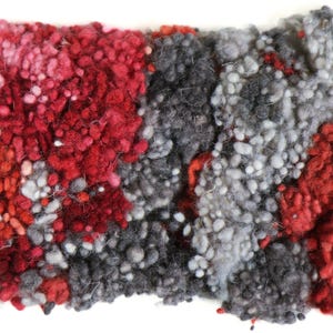 May include: A close-up of a textured fabric with a mix of red, pink, and gray colors. The fabric is made of small, round balls of yarn that are tightly woven together.