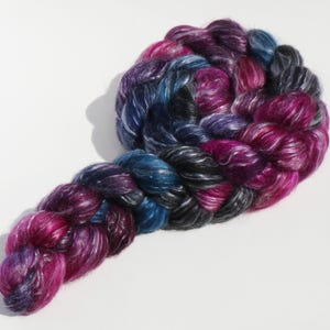 K&ouml;nnte beinhalten: Ein Strang handgef&auml;rbtes Garn mit einer bunten Farbpalette aus tiefem Magenta, K&ouml;nigsblau, Anthrazit und Schwarz. Die Faser hat einen ausgepr&auml;gten Glanz und ist zu einer dicken, geflochtenen Struktur mit sichtbarer Fasertextur verdreht.