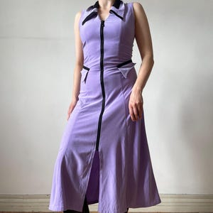 Puede incluir: Vestido sin mangas de color lavanda con cremallera y ribete negros. El vestido presenta un cuello y dos pequeños bolsillos. La modelo lleva botas negras. El vestido está hecho de un material suave y aterciopelado.
