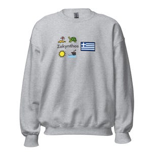 Könnte beinhalten: Ein meliertes graues Sweatshirt mit einem grafischen Design mit dem Wort "Zakynthos" und farbenfrohen Illustrationen eines Sonnenschirms, einer Schildkröte, einer Sonne, eines Bootes und der griechischen Flagge. Das Sweatshirt hat einen Rundhalsausschnitt und lange Ärmel.