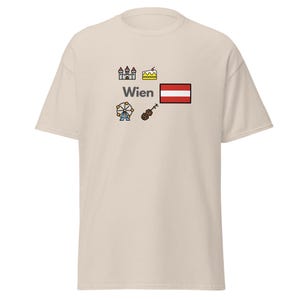 Könnte beinhalten: Ein hellbeige T-Shirt mit dem Wort "Wien" in Schwarz, begleitet von farbenfrohen Illustrationen eines Schlosses, Kuchens, Riesenrads, einer Geige und der österreichischen Flagge. Das Shirt ist aus weichem Material.