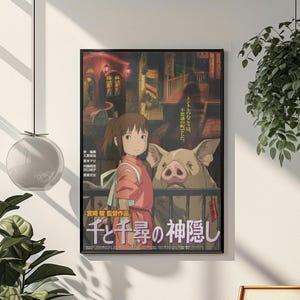 Op de afbeelding: Ingelijste poster met artwork uit de animatiefilm "Spirited Away". De poster toont een meisje in een rode outfit met een varken, met Japanse tekst. De poster wordt weergegeven op een witte muur.