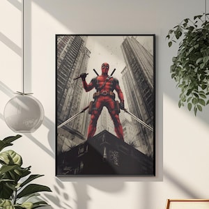 May include: Framed art print featuring Deadpool in a red and black costume, holding two swords, standing on a rooftop with a city backdrop. The artwork is displayed on a white wall, with a wooden chair and plants in the foreground.