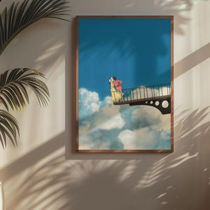 May include: A framed art print depicts a surreal scene of two figures on a bridge above clouds against a blue sky. The artwork features a brown frame and is displayed on a neutral-colored wall, with a potted plant in the foreground.