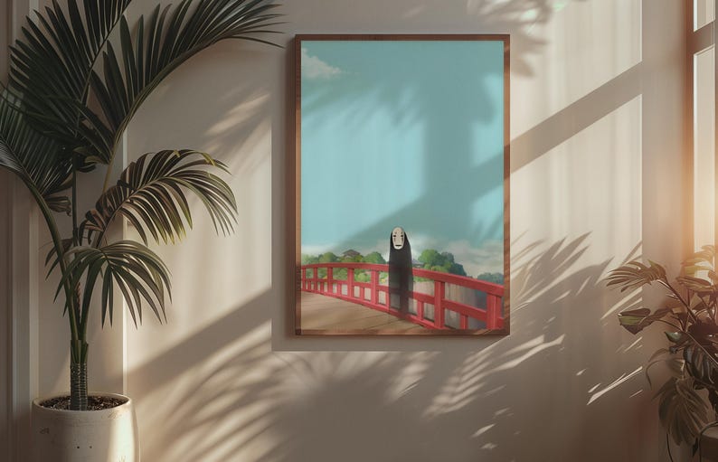 Op de afbeelding: Een ingelijste kunstdruk met een personage uit de animatiefilm Spirited Away. Het kunstwerk toont een figuur op een rode brug tegen een blauwe lucht. De print zit in een bruine lijst en wordt aan een beige muur getoond.