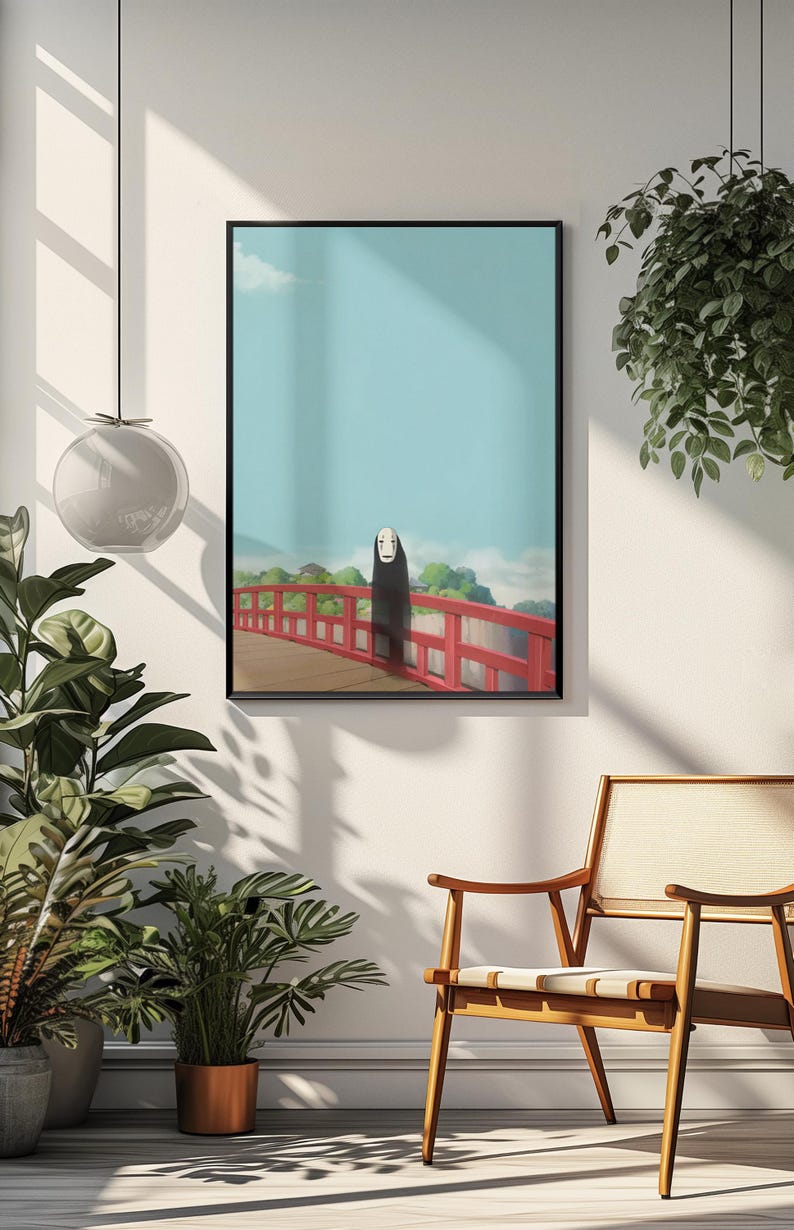 Op de afbeelding: Ingelijste kunstprint met een sc&egrave;ne uit de animatiefilm Spirited Away. Het kunstwerk toont een figuur in een zwarte mantel op een rode brug. De achtergrond toont een blauwe lucht en een groen landschap.