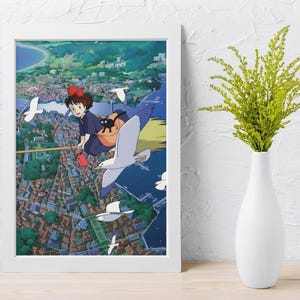 May include: A framed print of an anime scene featuring a young girl with a red bow flying on a broomstick with a black cat. The artwork is set against a backdrop of a coastal town with flying seagulls. The frame is white.