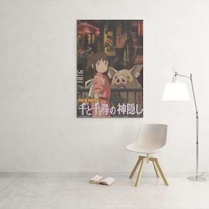Op de afbeelding: Een ingelijste poster met een sc&egrave;ne uit een animatiefilm. De afbeelding toont een jong meisje in een roze outfit en een varkensachtig wezen. Japanse tekst is zichtbaar onderaan. Een witte stoel, een boek en een lamp staan in de kamer.