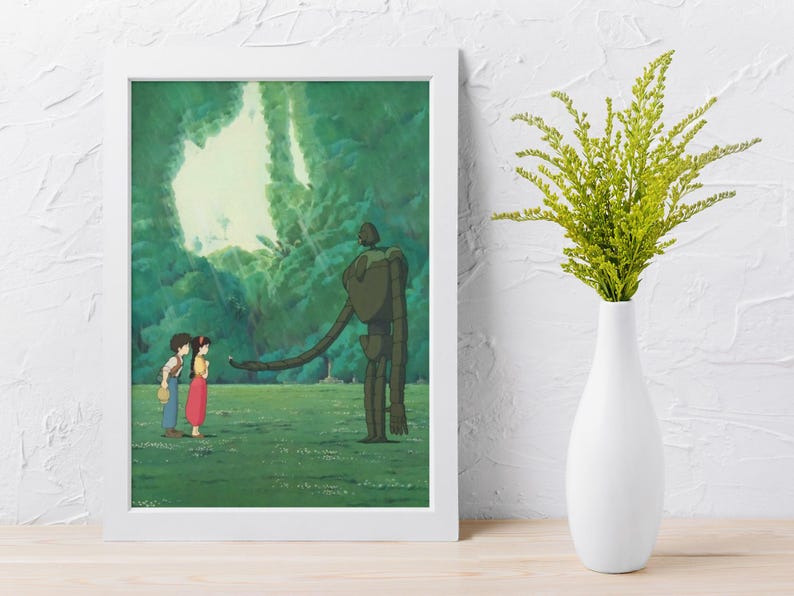 May include: A framed art print featuring an animated scene of two figures standing before a large, dark green robot in a grassy field. The background shows a bright, light-filled forest opening. The frame is white and rectangular in shape.